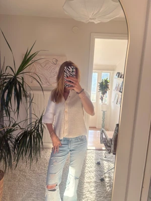 Vit stickad kofta med kort ärm - Säljer en söt vit stickad kofta med korta ärmar och v-ringning. Koftan har stora knappar framtill och är gjord i ett mjukt, fluffigt material. Perfekt att styla med jeans eller kjol för en chill look. Storlek xs, ginatricot 