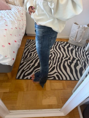 Blå bootcut jeans med slitningar - Säljer ett par blå bootcut jeans med snygga slitningar och tvättade detaljer. Jeansen har normal passform och klassiska bakfickor. Perfekta för dig som gillar en avslappnad men trendig stil.