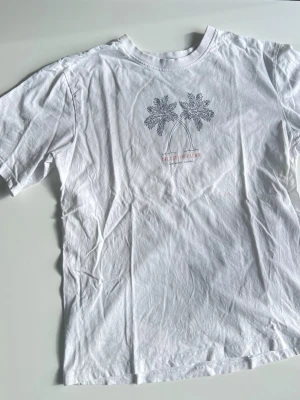 Vit t-shirt med palmer - Vit t-shirt  med tryck från Lager157. Oversized i passformen. En liten fläck precis ovanför palmerna som knappt syns (se bild).   Passform: Oversized.  Material: 100% bomull.  Brister: Liten prick (se bild)