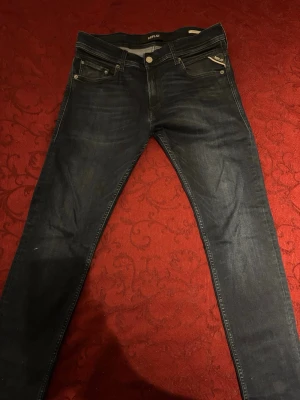 Mörkblå slim fit jeans från Replay - Snygga mörkblå slim fit jeans från Replay med klassisk femficksdesign och diskreta slitningar. Jeansen har en patch med Replay-logga bak i midjan och silverfärgade detaljer vid fickorna. Perfekta för en trendig och avslappnad stil. 💰 Pris: 1100kr (Priset kan självklart diskuteras vid en snabb och smidig affär!) 💬 Frågor? Tveka inte att skicka ett meddelande om du vill ha exakta mått, fler bilder eller vill lägga ett bud. Jag svarar snabbt!  