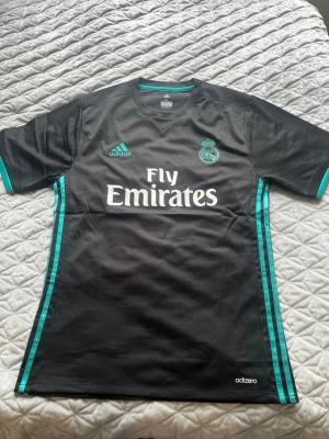 Real tredjetröja med isco - ✨ Real Madrid Tredjetröja – Isco #22 🖤🩵  Säljer en riktigt stilren och ikonisk svart/turkos Real Madrid-tröja med Isco 22 på ryggen! Tröjan är i Adizero-utförande med super snygga detaljer och har etiketten kvar 🏷️👌  🌟 Info om tröjan: 👕 Spelare: Isco #22 📏 Storlek: XL (True to size / Se bilder) 💎 Skick: Helt ny / Oanvänd! 🖤 Färg: Svart med snygga turkosa detaljer 🚚 Snabb Frakt: ⚡️ Skickas inom 24h – Frakttid 1-3 dagar.     📦💨                                                     Dm för frågor🫡