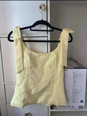 💛 Ljusgul topp med rosetter på axlarna – perfekt till sommaren - Söt ljusgul topp med fina rosettdetaljer på axlarna. Använd endast ett fåtal gånger och är i jättefint skick utan fläckar eller hål. Perfekt till jeans, kjol eller linnebyxor för en somrig och feminin look. 💛