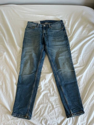 Blå raka jeans  - Säljer ett par klassiska blå jeans med raka ben och snygga slitningar på framsidan. Jeansen har fem fickor, knappgylf och kontrastsömmar. Perfekta till en avslappnad stil och tillverkade i bomullsdenim.