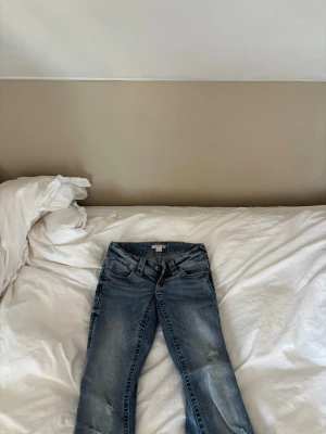 Blå jeans med paljettdetaljer - Säljer ett par blå jeans med snygga slitningar och paljettdetaljer på bakfickorna. Jeansen har klassisk femficksmodell, normal midja och raka ben. Perfekta för dig som vill ha något extra till din denimlook. Jeans är helt slut sålda så passa på🤏💕