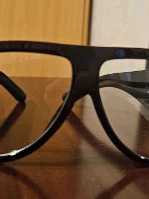 Svarta solglasögon med bred båge - Stilrena svarta solglasögon med bred, glansig båge och diskret metall-detalj vid skalmen. Klassisk rektangulär form som ger en cool vibe och passar till många looks. Perfekta för dig som vill ha en enkel men trendig accessoar.