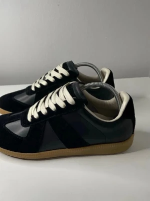 Svarta sneakers med beige sula - Snygga svarta sneakers med beige gummisula och vita skosnören. Ovandelen är i en mix av mocka och slätt läder för en cool kontrast. Klassisk låg modell som passar till det mesta och ger en clean look.