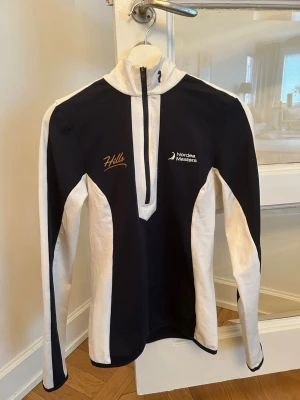 Hills peak performance  - Snygg svart och vit långärmad träningströja med halv dragkedja framtill. Tröjan har Nordea Masters-logga och texten 'Hills' broderat på bröstet. Perfekt för träning eller sportiga aktiviteter, med skön passform och sportig design. Liten i storlek.