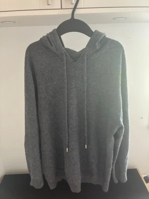 Kashmir hoodie mörkgrå - Enkel och stilren grå hoodie med huva och dragsnören. Tillverkad i ett mjukt, stickat material som känns skönt mot huden. Hoodien har långa ärmar och ribbade muddar vid ärmslut och nederkant. Perfekt för en avslappnad look. Passar någon som är ca 180 cm. Skriv vid frågor!