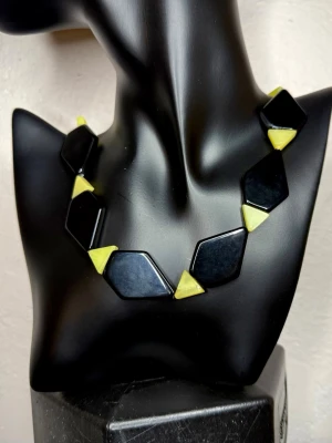Unikt Handgjort Modernistiskt Retrohalsband 60/70-tal Svensk Studiodesign Statement Oanvänt - Ovanligt handgjort statementhalsband med grafisk, modernistisk 60/70-talskänsla. Kommer från kvarvarande lager efter en svensk kvinnlig smyckekonstnär som arbetade småskaligt och skapade unika smycken. De svarta delarna uppfattas som glas och de gulgröna som natursten, men materialen är inte verifierade. Längd ca 52 cm, största delar ca 2,5 cm. Oanvänt och i mycket fint skick. Bundlerabatt vid köp av flera varor.