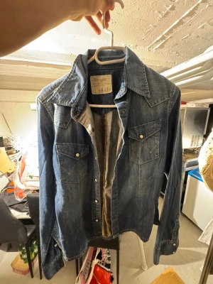 Klassisk blå jeansjacka med fickor - Snygg blå jeansjacka med två bröstfickor med lock och tryckknappar. Jackan har en klassisk krage, långa ärmar med manschett och tryckknappar framtill. Perfekt för dig som gillar en tidlös och avslappnad stil.
