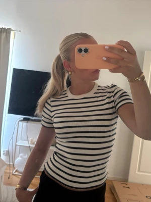 Randig ribbad topp  - Säljer en kortärmad, ribbad topp med svarta och vita ränder. Toppen har en rund halsringning och sitter tight mot kroppen. 