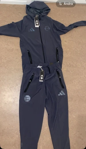 Mörkblå träningsset från Adidas - Snyggt mörkblått träningsset från Adidas med både jacka och byxor. Setet har dragkedjor på jackan och byxorna, huva med snörning och Bayern München-logga på både överdel och underdel. Perfekt för träning eller chill. Materialet är lätt och andas.jackan xs byxor S hjälper en vän att sälja fotbolls dressen 