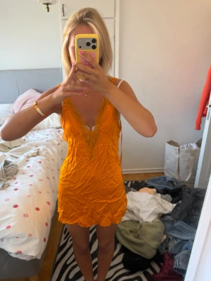 Orange klänning med spetsdetaljer - Snygg  orange klänning med djup V-ringning och spetsdetaljer vid urringningen. Kort modell med tunna axelband och mjukt, glansigt tyg som ger en lyxig känsla. 
