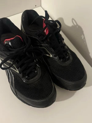 Svarta Reebok sneakers med mesh - Säljer ett par svarta Reebok sneakers med mesh-ovandel och detaljer i silver och rosa. Skorna har klassisk snörning och låg profil. Perfekta för dig som gillar sportig stil och vill ha bekväma skor till vardags.
