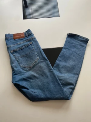 Blå jeans i modellen Evolve 33/32 - Säljer ett par klassiska blå jeans i modellen Evolve. Jeansen har fem fickor, normalhög midja och raka ben. Tillverkade i ett slitstarkt denimtyg med snygga kontrastsömmar och en brun patch bak i linningen.