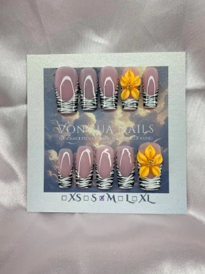 Fauve (M);Medium Square - Snygga handgjorda press-on naglar i en medium lång square med nude bas, handmålade vita franska tippar med zebramönstrad. Två naglar har handgjorda 3D-gula/orange blommor med guld pärlor i mitten för extra wow-effekt. Perfekt för dig som vill sticka ut med trendiga och kreativa naglar.M: 16 mm, 12 mm, 12,5 mm, 11,5 mm, 10 mm