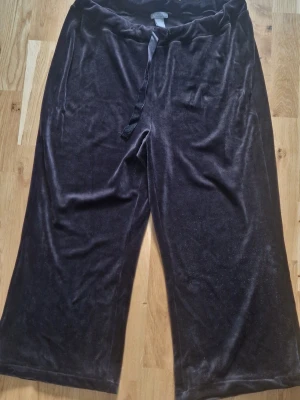Mjukisbyxor i velour - Mysiga svarta mjukisbyxor i mjuk velour med breda ben och snören i midjan (på ena sidan har snöret åkt in) Perfekta för chill dagar hemma eller när du vill vara extra bekväm. Klassisk look med enkel design och skön passform.