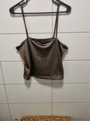 Brun ribbad linnetopp från BikBok - Snygg brun ribbad linnetopp från BikBok med tunna axelband och croppad passform. Tillverkad i ett mjukt och glansigt material som ger en lyxig känsla. Perfekt att styla med jeans eller kjol för en trendig look.