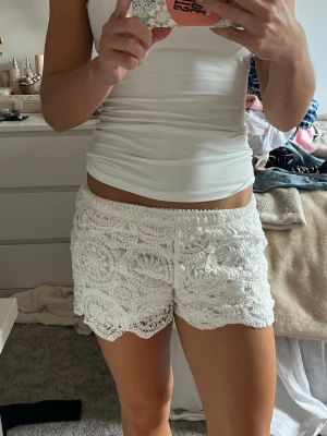 Vita virkade shorts med spetsdetaljer - Säljer ett par vita virkade shorts med fina spetsdetaljer och scallop-kant. De är lågmidjade och har en avslappnad passform, perfekta för sommardagar. Materialet känns luftigt och mjukt, vilket gör dem riktigt sköna att bära. De är aldrig använda då de är lite för små för mig.
