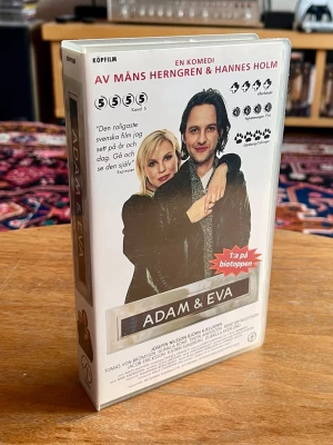 Adam & Eva (1997) VHS - Helt NY och INPLASTAD! - Klassisk svensk romantisk dramakomedi från 1996 av Måns Herngren och Hannes Holm, med Björn Kjellman och Josefin Nilsson i huvudrollerna.  Detta är ett unikt exemplar för samlaren – filmen är helt ny, oanvänd och fortfarande i sin originalplast (inplastad köpfilm).  - Format: VHS  - Skick: Ny/Inplastad (Se bilder för skick på plast/fodral)  - Genre: Komedi / Romantik  - Språk: Svenska  Skickas väl emballerat. Kika gärna på mina andra produkter för samfrakt!