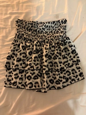 Leopardmönstrad kortkjol med volang - Säljer en kort kjol med leopardmönster i svart och vitt. Kjolen har smock i midjan och dubbla volanger som ger en snygg och trendig look. Perfekt för dig som vill sticka ut lite extra.