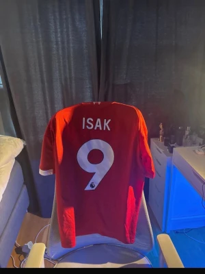 Liverpool röd matchtröja ISAK 9 - Säljer en röd Liverpool matchtröja med ISAK och nummer 9 på ryggen. Tröjan har vita detaljer, klubbmärke och sponsorloggor på bröstet samt vita ränder på axlarna. Qr cod kan scannas för att komma direkt till adidas hemsida och påse skickas självklart med skriv om ni undrar något!!