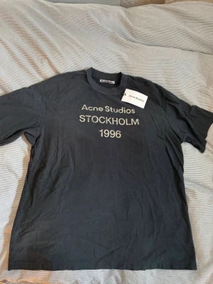 Svart Acne Studios t-shirt - Cool svart t-shirt från Acne Studios med trycket 'Acne Studios STOCKHOLM 1996' på bröstet. Klassisk rund hals och korta ärmar. Perfekt för dig som gillar stilrena och trendiga plagg med streetkänsla.