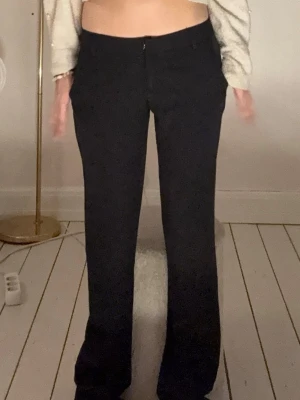 Svarta utsvängda kostymbyxor - Snygga svarta kostymbyxor med utsvängda ben och medel midja. Byxorna har en klassisk dragkedja framtill och sitter tight över höfterna för en clean look. Perfekta för dig som gillar stilrena och trendiga plagg.