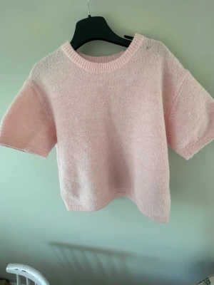 Ljusrosa stickad t-shirt - Söt ljusrosa stickad t-shirt med korta ärmar och rund halsringning. Tröjan har en mjuk och fluffig känsla, perfekt för en avslappnad och trendig look. Passar bra till både jeans och kjol.