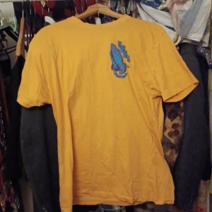 Vintage t-shirt med tryck från Santa Cruz - Cool gul t-shirt från Santa Cruz med ett stort färgglatt tryck av en religiös ikon på baksidan och texten 'Pray for Me' på framsidan. Perfekt för en avslappnad stil med en touch av streetwear. Passar bra till jeans eller shorts för en chill look.