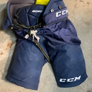 Blå hockeybyxor från CCM - Säljer ett par blå hockeybyxor från CCM i storlek Junior Large. Byxorna har en robust design med justerbar snörning och bälte för perfekt passform. Perfekta för hockeyträning eller match. De är i bra skick och redo för isen!