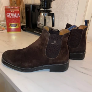 Gant boots - Säljer ett par snygga bruna Chelsea boots från Gant i mocka. De har en klassisk design med elastiska paneler på sidorna för enkel på- och avtagning. Perfekta för både höst och vår! Skorna är i bra skick och redo för nya äventyr.