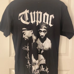 Svart T-shirt med Tupac-tryck - Cool svart T-shirt med stort Tupac-tryck på framsidan. T-shirten är kortärmad och i bra skick. Den är i storlek xs men är stor i storleken så den passar S mycket bra 