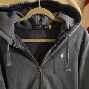 Ralph Lauren Zip Hoodie (Blå) - Tja, säljer nu min knappt använda Ralph lauren Zip-Hoodie 50% billigare än nypris. Använd fåtal gånger då jag tycker att M är för stort för mig. Hoodien är i väldigt bra skick och har använts varsamt och försiktigt, och är köpt från Zalando. Pris kan diskuteras vid snabb affär! Ny pris ligger på 2199 kr! 