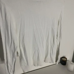 Vit långärmad tröja - Säljer en enkel och stilren vit långärmad tröja. Perfekt för lager-på-lager under höst och vinter. Tröjan har ribbade muddar vid ärmsluten för en bekväm passform. Passar både till vardags och mer uppklädda tillfällen.