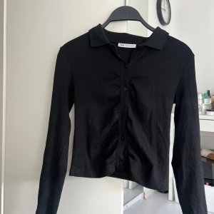 Svart ribbad tröja från Zara - Säljer en stilren svart ribbad tröja från Zara i storlek M. Tröjan har långa ärmar och knappar framtill, perfekt för både vardag och fest. Den är i bra skick och passar till alla säsonger. Ett måste i garderoben! 🖤