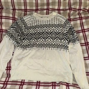 Vit och svart mönstrad tröja från GAP - Säljer en snygg vit tröja från GAP med svart geometriskt mönster över bröstet och axlarna. Perfekt för kyliga dagar med sin långärmade design. Tröjan är i bra skick och passar både till vardags och lite finare tillfällen. Skön och stilren💞! vinterfin!