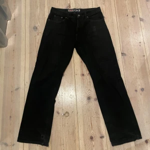 Svarta jeansbyxor från Jinglers - Säljer ett par svarta jeansbyxor från Jinglers i använt skick med slitage längs ner på benen.  De har en klassisk straight passform. Storlek 33/32