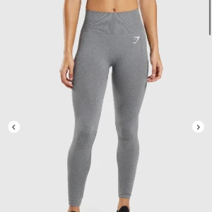 Grå leggings från Gymshark - Säljer ett par grå leggings från Gymshark i mycket bra skick. De är högmidjade och har en tight passform, perfekt för träning. Materialet är stretchigt och bekvämt, med ett diskret mönster och Gymshark-loggan på låret. Perfekta för gymmet eller yoga!