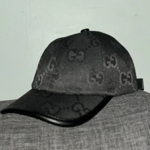 Svart keps från Gucci - Säljer en snygg svart keps från Gucci med deras ikoniska GG-mönster. Kepsen är i mycket bra skick och har en justerbar rem baktill för perfekt passform. Tillverkad i Italien med högkvalitativt material. Perfekt för både vardag och fest!