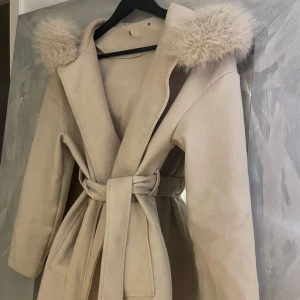 Beige kappa med luva - Säljer en superfin beige kappa med luva och knytskärp i midjan. Den har långa ärmar och två praktiska fickor fram. Kan gå ner i pris vid snabb affär:) 