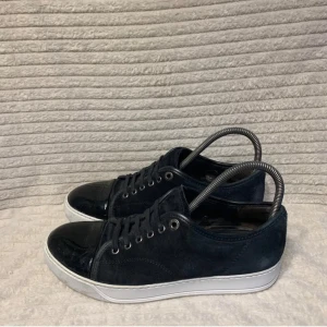 Lanvins - Snygga svarta sneakers från Lanvin i mocka och skinn. De har en stilren design med snörning och en vit sula som kontrasterar snyggt mot det svarta. Perfekta för både vardag och fest! Skorna är i mycket bra skick och redo för nya äventyr och jag säljer för att de sitter för små för mig!. UK 5