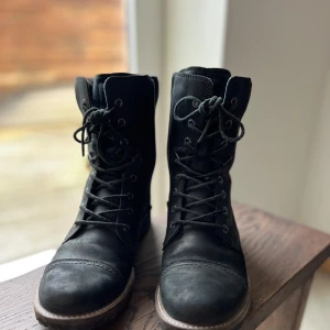 Svarta Ecco boots med snörning och dragkedja - Säljer ett par snygga svarta boots i skinn med både snörning och dragkedja på sidan. De har en robust sula och en liten klack, perfekt för höst och vinter. Bootsens stilrena design gör dem lätta att matcha med olika outfits. Använda men i bra skick.