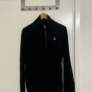 Svart långärmad tröja från G-Star RAW - Säljer en stilren svart långärmad tröja från G-Star RAW i storlek L. Tröjan har en praktisk dragkedja vid halsen och är perfekt för både vardag och lite kyligare dagar. Den är i mycket bra skick och redo för en ny ägare!