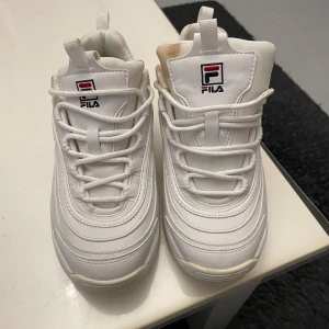 Vita sneakers från Fila - Säljer ett par vita Fila sneakers i bra skick. De har en klassisk design med snörning och Fila-loggan på sidan och tungan. Perfekta för vardagsbruk och ger en sportig look. Skorna är bekväma och har en robust sula för extra stöd. Enda problemet är att det har spilts kaffe på ena skorn annars har dom användas 1-2 gånger och är därför fräscha förutom olyckan😬 Passar både killar och tjejer, priser går alltid att diskutera🤩