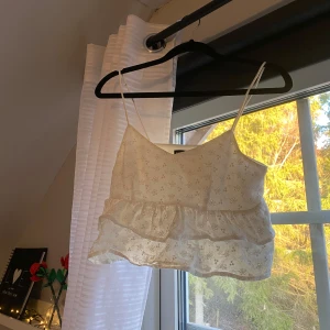 Vit blommig topp från Shein - Söt vit topp från Shein i storlek XS. Den har tunna axelband och ett blommigt mönster. Toppen är croppad med volangdetaljer, perfekt för sommardagar. Använd ett fåtal gånger🌟
