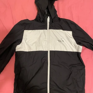 Svart och vit vindjacka från Puma - Säljer en snygg svart och vit vindjacka från Puma. Jackan har en dragkedja framtill och en huva för extra skydd mot väder. Perfekt för vår och höst när det blåser lite extra. Den är i mycket bra skick och redo för nya äventyr! Passar både killar och tjejer, priser går alltid att diskutera🤩