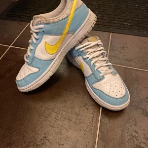 Nike Dunk i blått och gult - Säljer ett par Nike Dunk i fräscht blått och vitt med gul . Skorna har snörning och är i bra skick, perfekta för både vardag och fest. De har en klassisk design med perforerad tå för extra ventilation.