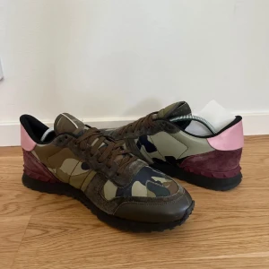 Valentino Garavani sneakers i camouflage - Säljer ett par snygga Valentino Garavani sneakers i camouflage. De har en cool mix av gröna och bruna nyanser med rosa detaljer på hälen. Skorna har snörning och är i bra skick. Säljer på grund av att dom är för stora. Nypris 7000 kr säljer för 2799