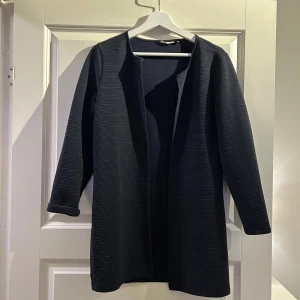 Svart kappa - Snygg svart kappa med långärmad design och en stilren look. Perfekt för att hålla stilen i kyligare väder. Den har en enkel och elegant form som passar till många olika outfits.
